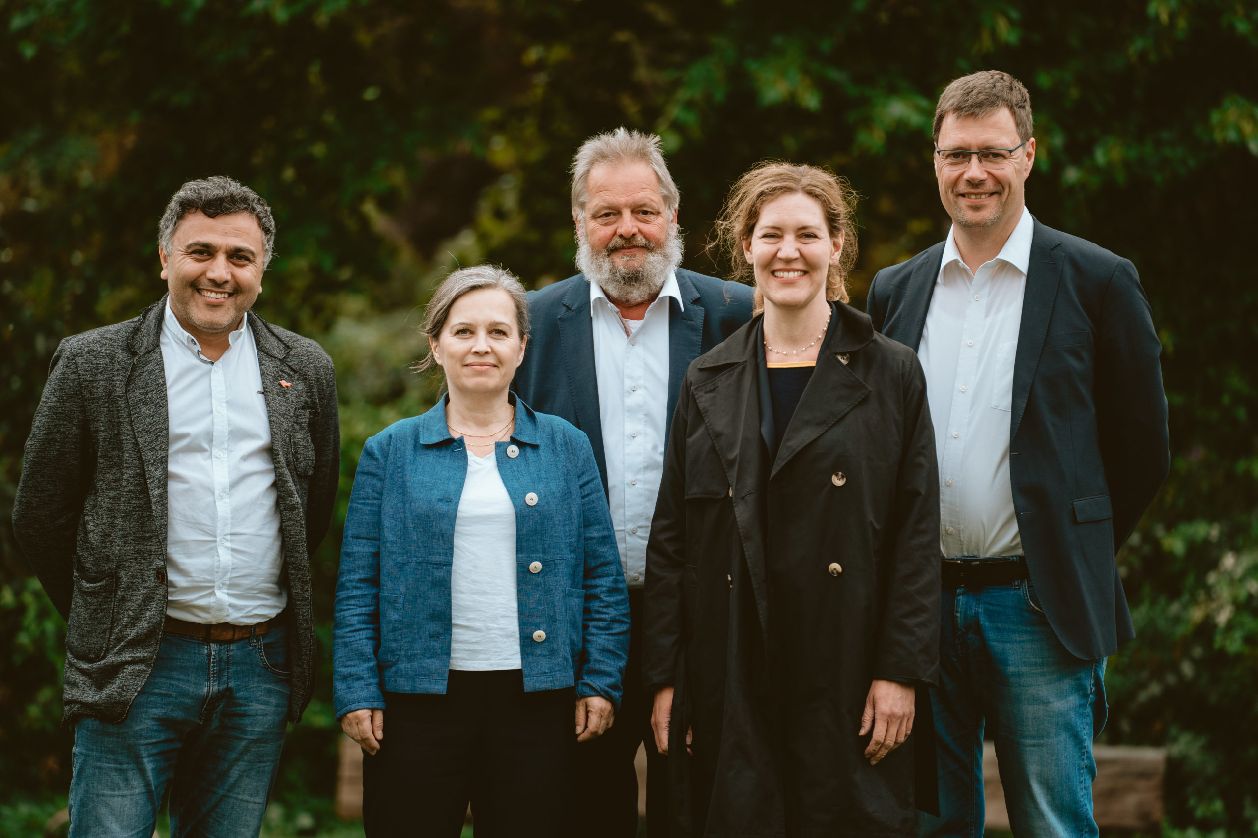 weitere fünf Personen stehen vor grünem Hintergrund