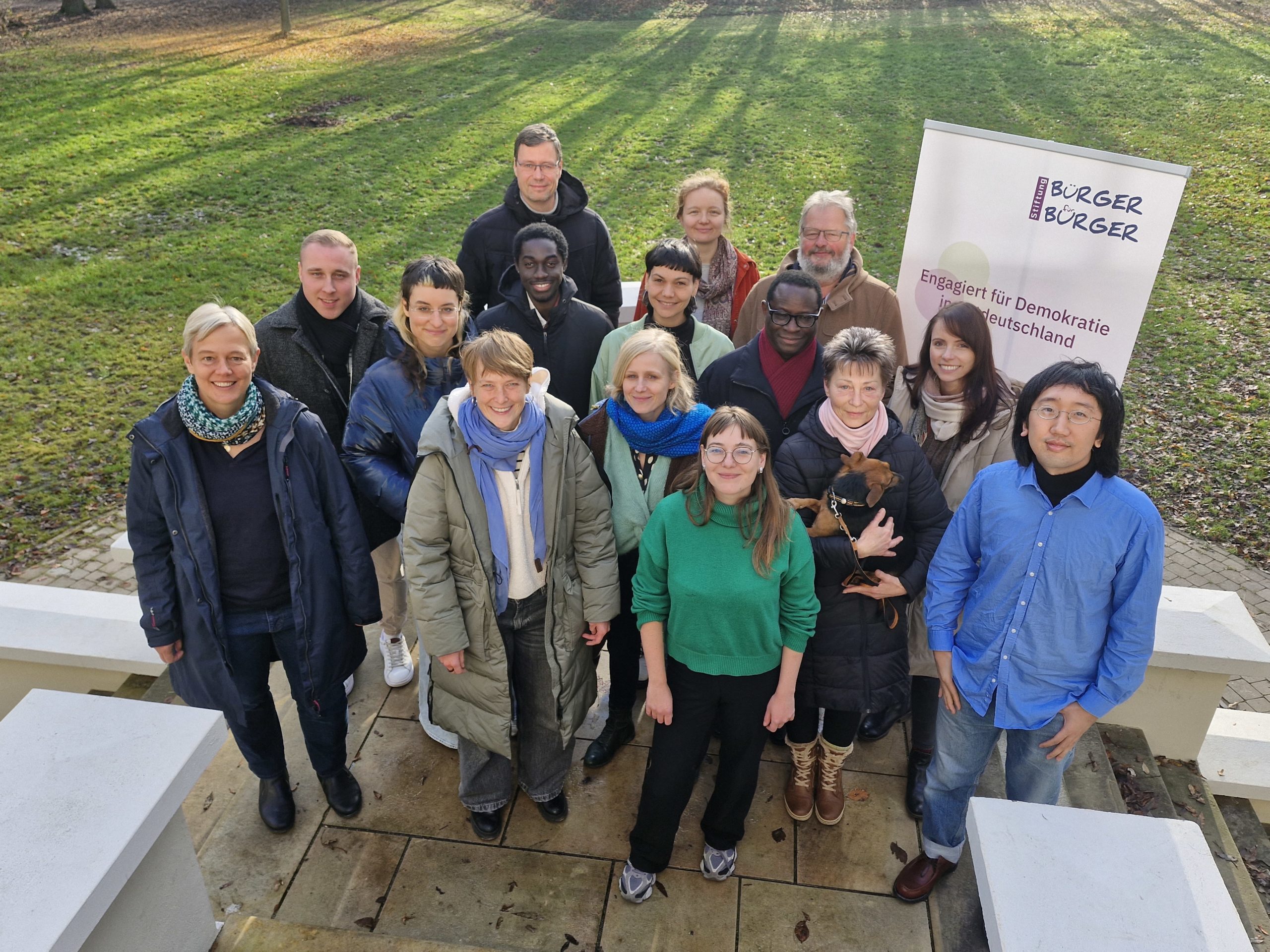 Eine Gruppe von Menschen steht im freien vor einem Roll-up der Stiftung Bürger für Bürger
