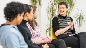 eine Frau sitzt auf einem Stuhl und spricht mit drei ihr zugewandten Personen