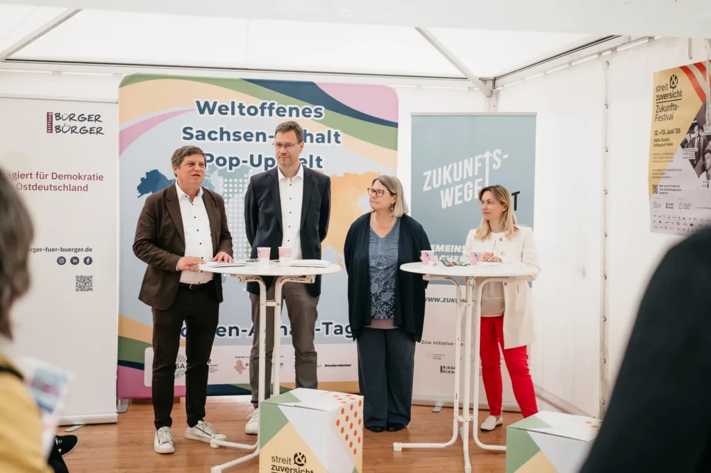 zwei Männer und zwei Frauen stehen n Stehtischen vor Roll-ups